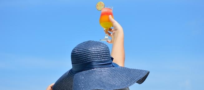 person in sunhat raising a cocktail in the air