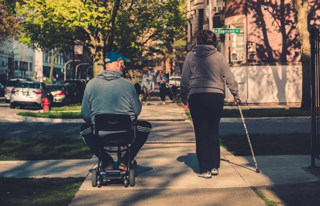 person in wheelchair and person with walking cane crossing street